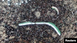 Des gens portent des drapeaux de l'opposition lors d'une manifestation marquant le 10e anniversaire du début du conflit syrien, à Idlib, en Syrie, le 15 mars 2021.