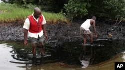 FILE - Men walk in an oil slick covering a creek near Bodo City in the oil-rich Niger Delta region of Nigeria, June 10, 2010.