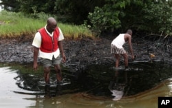 FILE - Men walk in an oil slick covering a creek near Bodo City in the oil-rich Niger Delta region of Nigeria, June 10, 2010.