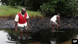 Photo d'archives: Des hommes marchant dans une nappe de pétrole couvrant un ruisseau près de la ville de Bodo dans la région du delta du Niger, 10 juin 2010.