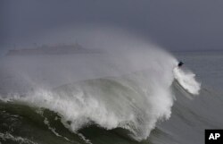 A surfer rides a wave near Fort Point in front of Alcatraz Island in San Francisco, , Nov. 29, 2018. A storm moving into California brought rain that may bring snow and cause travel problems in the Sierra Nevada mountains.