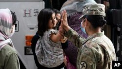FILE - Army Pfc. Kimberly Hernandez gives a high-five to a girl evacuated from Kabul, before boarding a bus after they arrived at Washington Dulles International Airport, Aug. 30, 2021.