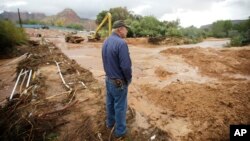 Following a flash flood that killed at least 15 people, a man looks on as crews clear mud and debris from a road in Colorado City, Ariz., which adjoins Hildale, Utah, Sept. 15, 2015.