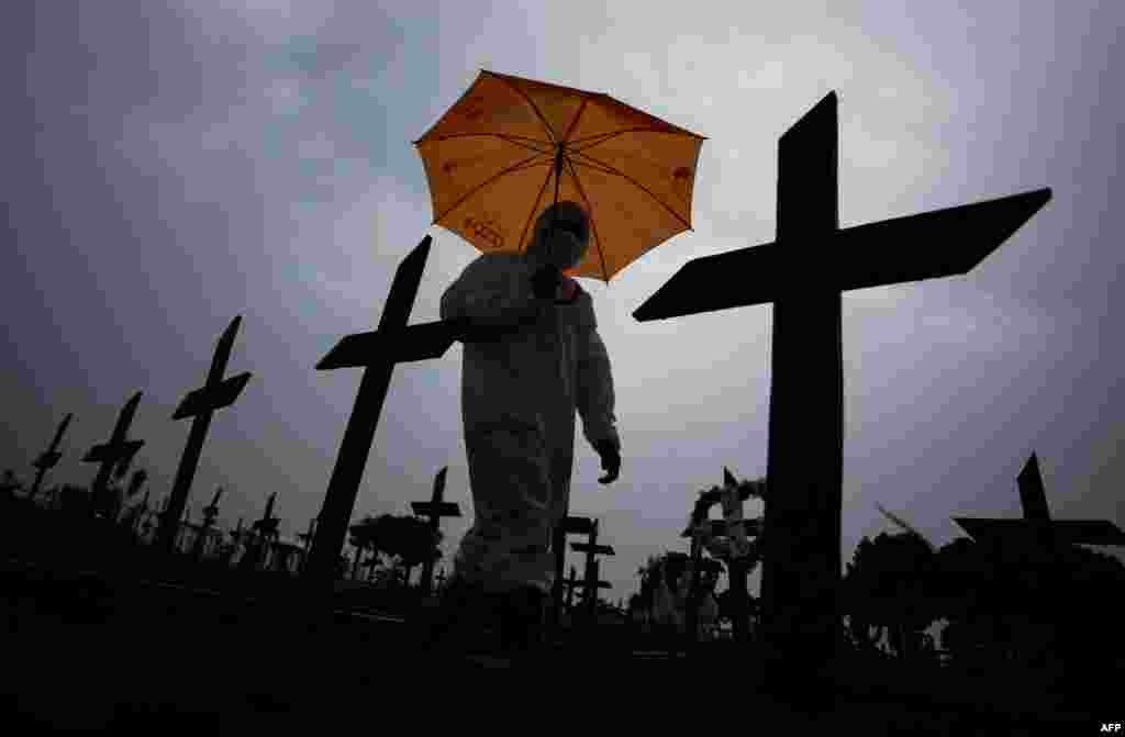 A worker wearing a protective suit and carrying an umbrella walks past the graves of COVID-19 victims at the Nossa Senhora Aparecida cemetery, in Manaus, Brazil.