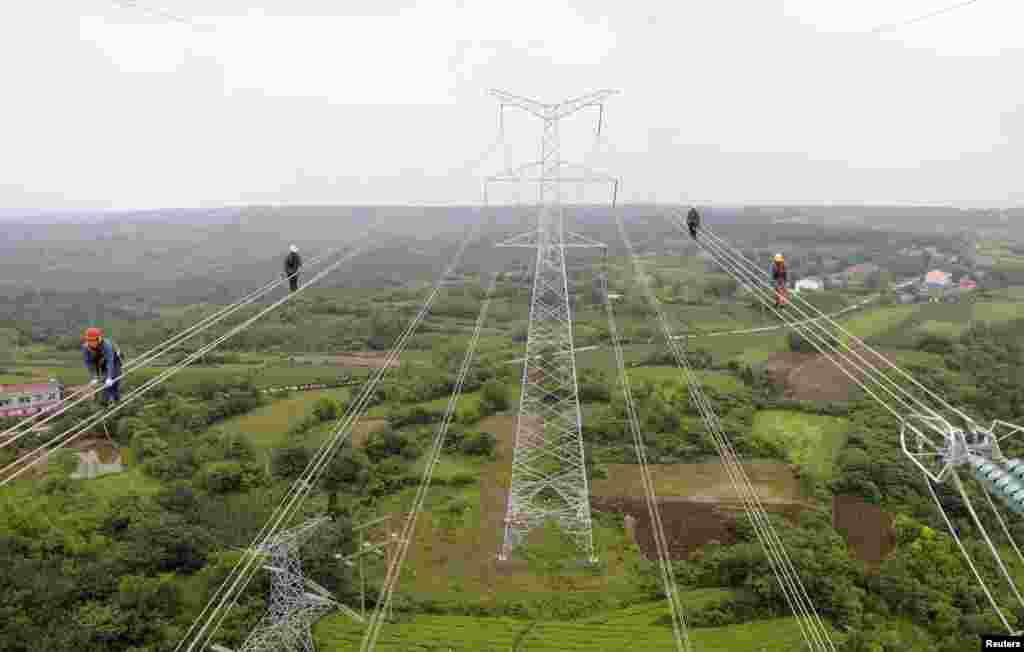 Workers walk along wires as they inspect newly-built electricity pylons above crop fields in Chuzhou, Anhui province, China.