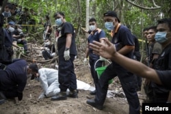 Policemen monitor as forensic experts dig out human remains near the abandoned human trafficking camp in the jungle close the Thailand border at Bukit Wang Burma in northern Malaysia May 26, 2015. Malaysian police forensic teams, digging with hoes and sho