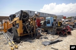 FILE - In this May 3, 2021 file photo, a man rests in the shade of destroyed machinery sold by the US military to a scrapyard, outside Bagram Air Base, in Afghanistan. (AP Photo/Rahmat Gul, File)