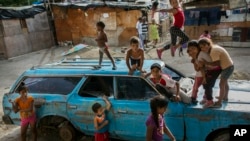 FILE - Children play on top of an abandoned car at the "Aguerridos Liberator" shanty town in Caracas, Venezuela, May 9, 2019. 