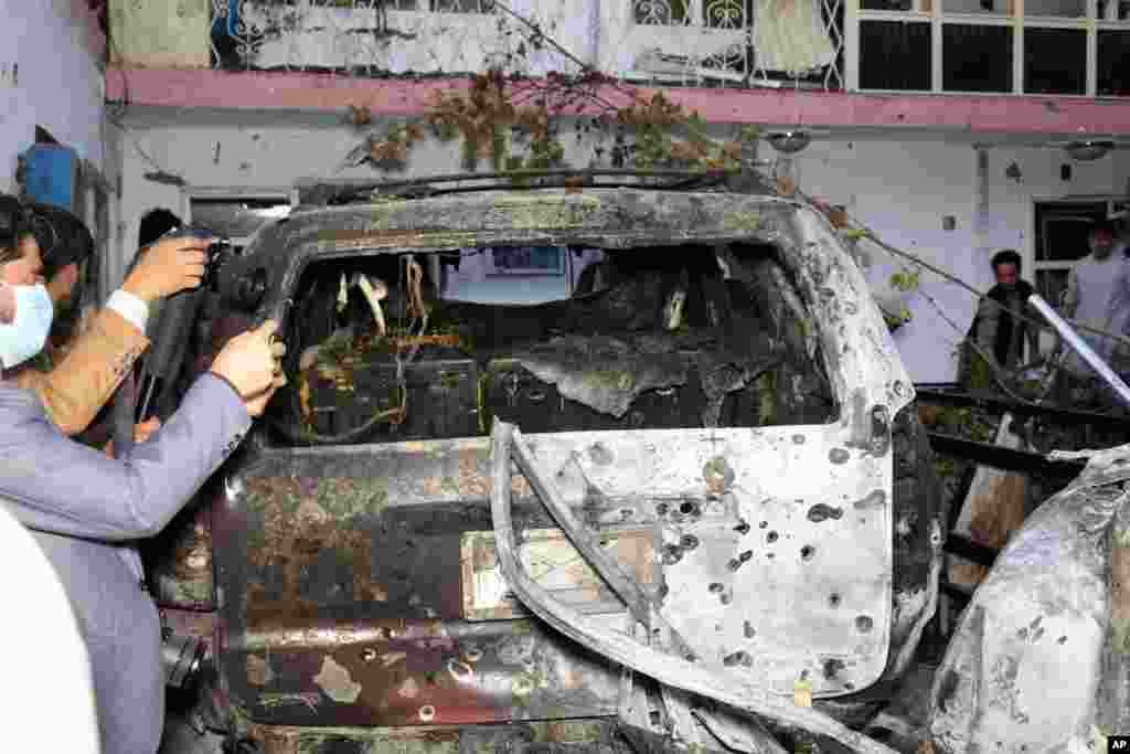 Afghan journalists take a photos of destroyed vehicle inside a house after U.S. drone strike in Kabul. A U.S. drone strike destroyed a vehicle carrying "multiple suicide bombers" from Afghanistan's Islamic State affiliate.
