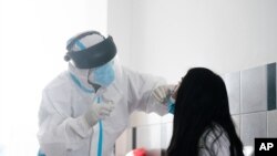 Un trabajador de la salud vestido con equipo de protección en medio de la nueva pandemia de coronavirus, toma una muestra de hisopo nasal de una mujer para realizar la prueba de COVID-19, el 6 de enero de 2021.