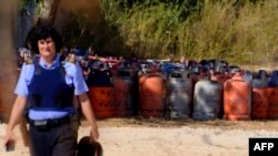 FILE - A policewoman walks with dozen of gas bottles in background in Alcanar during a search linked to the Barcelona and Cambrils attacks on the site of an explosion on Aug. 18, 2017.