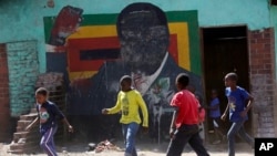 Children play soccer next to a defaced portrait of former Zimbabwean President Robert Mugabe in Harare, Sept, 6 2019.