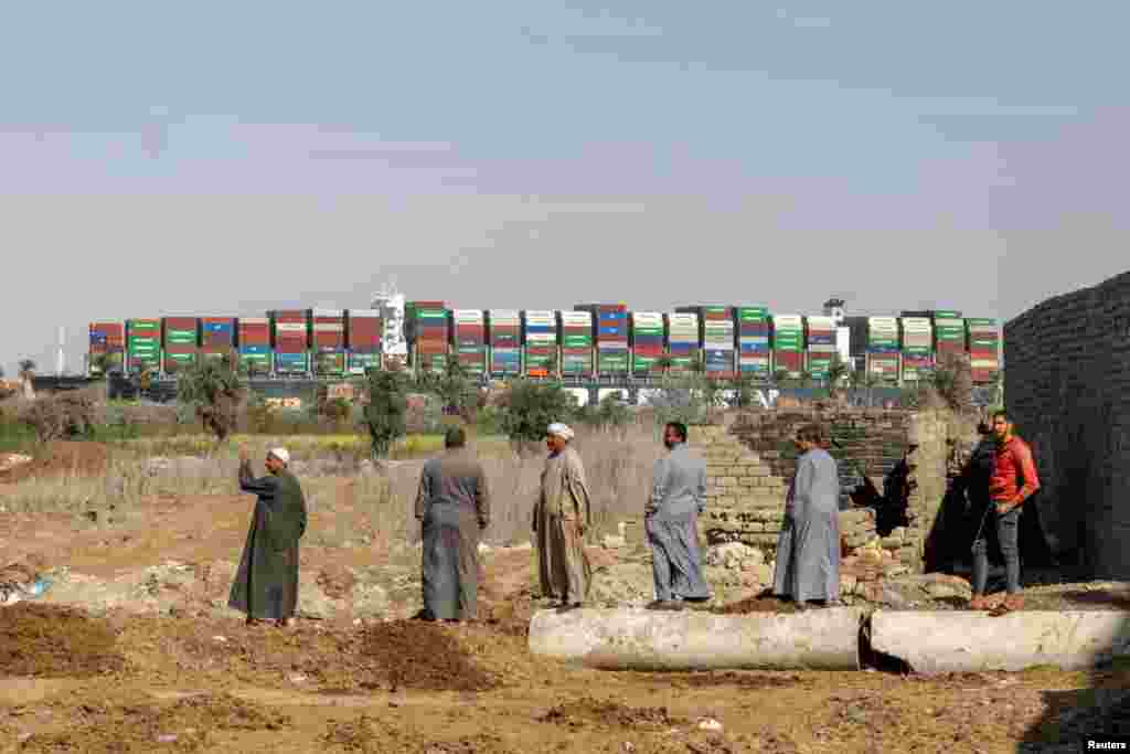 People gather as ship Ever Given, one of the world&#39;s largest container ships, is seen in Suez Canal, Egypt. The 400-meter ship that had been blocking the canal has been freed and is making its way down the waterway.