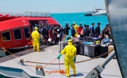 In this photo released by the Indonesian military, personnel in protective suits help unload belongings of Indonesian crew members from the World Dream cruise ship as they are transferred to a hospital ship near Durian Bay, Indonesia, Feb. 26, 2020.