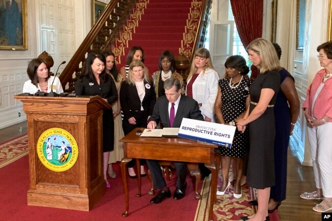 North Carolina Democratic Gov. Roy Cooper signs an executive order designed to protect abortion rights in the state at the Executive Mansion in Raleigh, N.C. on Wednesday, July 6, 2022. The order in part prevents the extradition of a woman who receives an abortion in North Carolina but may live in another state where the procedure is barred. (AP Photo/Gary D. Robertson).