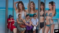 FILE - Four women wait at a bus stop in front of an advertising poster for swimwear and beach wear in Madrid, Spain, May 27, 2017. The head of the U.N. for Women is urging advertisers to eliminate such stereotypes in their ads.