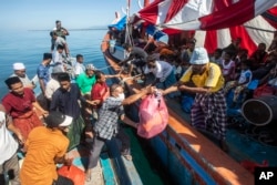 Warga Aceh (kiri), membagikan barang-barang bantuan untuk Muslim Rohingya yang terdampar di atas perahu yang berlabuh di perairan dekat pantai Labuhan Haji, provinsi Aceh, 23 Oktober 2024. (Binsar Bakkara/AP)