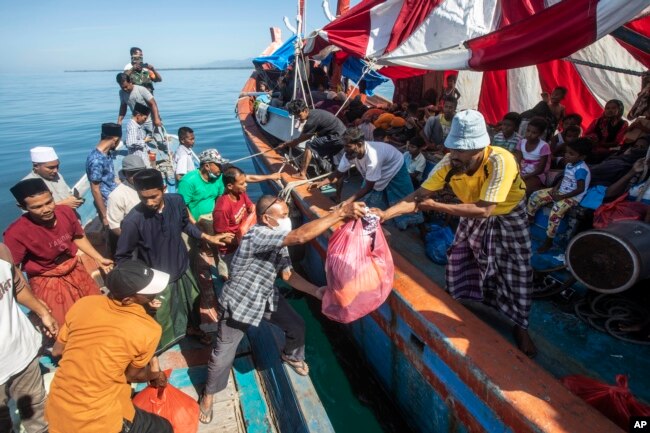 Warga Aceh (kiri), membagikan barang-barang bantuan untuk Muslim Rohingya yang terdampar di atas perahu yang berlabuh di perairan dekat pantai Labuhan Haji, provinsi Aceh, 23 Oktober 2024. (Binsar Bakkara/AP)