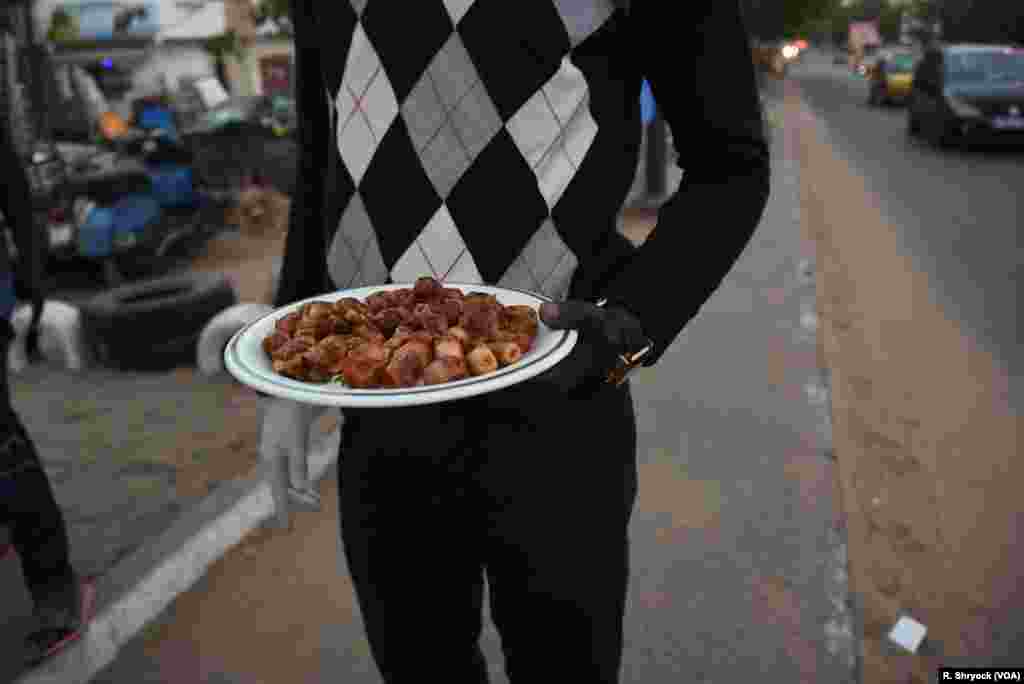 A man hands out dates to taxi drivers and bus passengers along a busy street in Dakar, Senegal, May, 23, 2018, as the sun sets.&nbsp;Devout Muslims break the fast in Senegal as they prepare large quantities of food and drink to share with those around them.&nbsp;