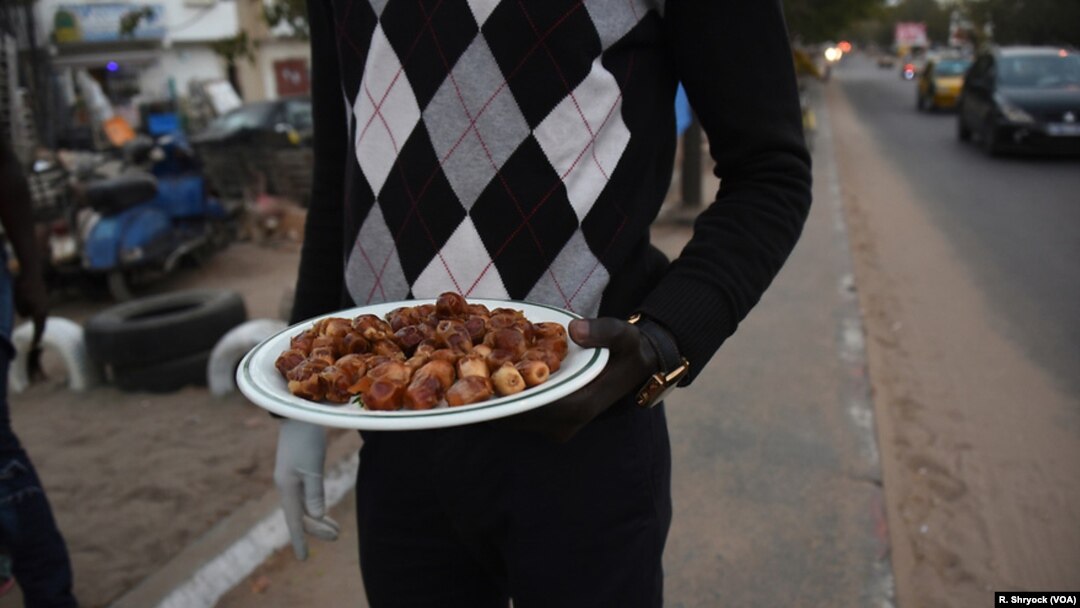 Seorang pria membagikan kurma kepada pengemudi taksi dan penumpang bus di sepanjang jalan yang sibuk di Dakar, Senegal, 23 Mei 2018, saat matahari terbenam dan saatnya berbuka puasa selama Ramadan. (Foto: VOA)