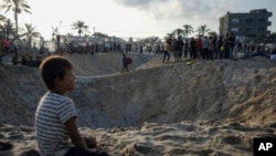 FILE - Palestinians look at the destruction after an Israeli airstrike on a crowded tent camp housing Palestinians displaced by the war in Muwasi, Gaza Strip, Sept. 10, 2024.