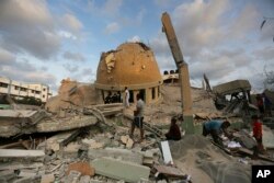 Orang-orang berdiri di luar masjid yang hancur akibat serangan udara Israel di Khan Younis, Jalur Gaza, Minggu, 8 Oktober 2023. (Foto: AP)