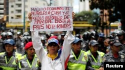 FILE - A woman holds a sign that reads: "Maduro gives oil to Cuba and people die of hunger. Enough. Country do not give up" during a protest in Caracas, Venezuela, Aug. 16, 2018. 