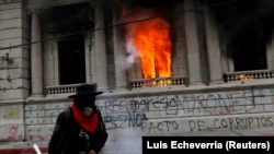Seorang pria berjalan melewati kantor gedung Kongres yang dibakar oleh demonstran selama protes menuntut pengunduran diri Presiden Alejandro Giammattei, di Guatemala City, Guatemala 21 November 2020. (Foto: REUTERS/Luis Echeverria)