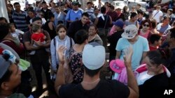 In this June 13, 2018 photo, an organizer, foreground, speaks to families as they wait to request political asylum in the United States, across the border in Tijuana, Mexico. 