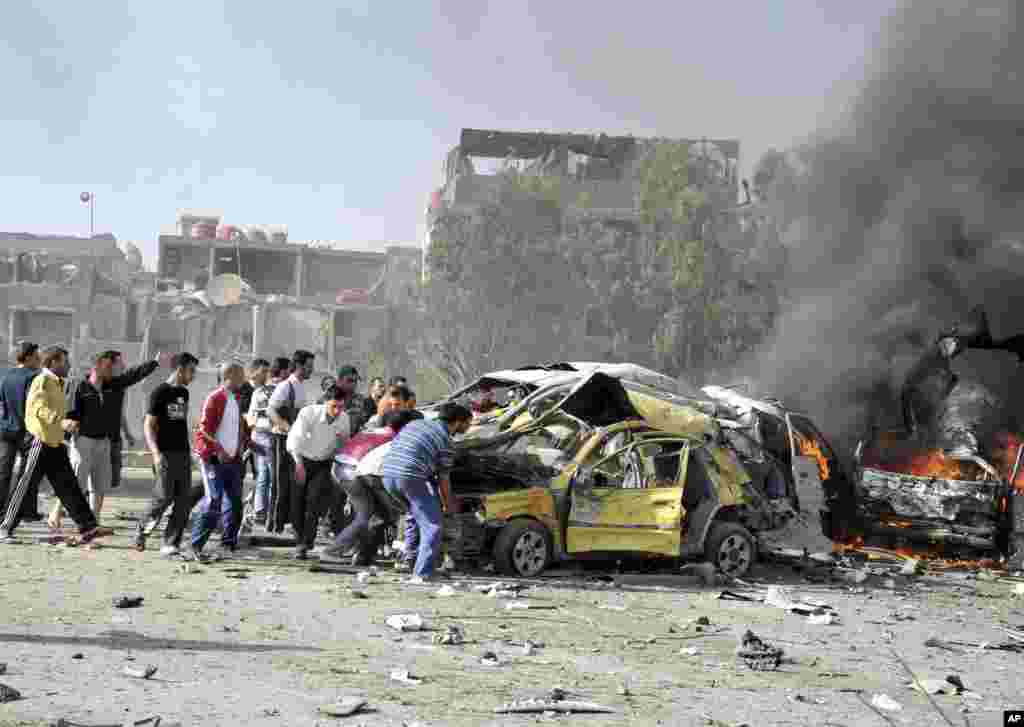 People and security personnel try to remove a car from an explosion site in Damascus. 
