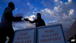 FILE - A county worker collects mail-in ballots in a drive-thru ballot drop off area at the Clark County Election Department in Las Vegas, Nov. 2, 2020. A new law in Nevada for 2022 requires that all registered voters receive a ballot by mail for each election.