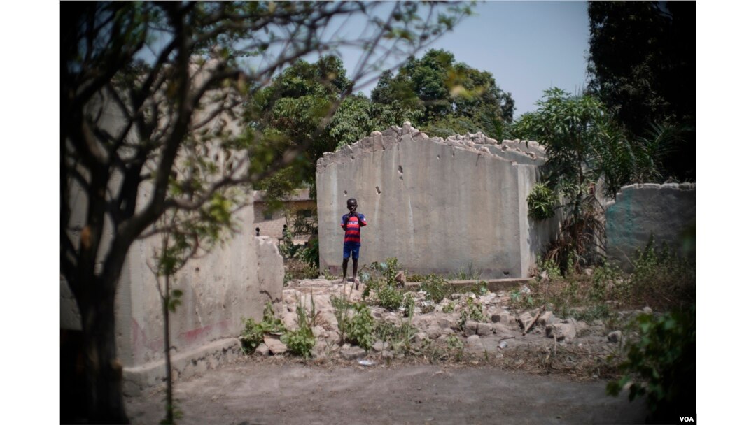 A young boy stands next to the shell of a home that was destroyed in the PK5 neighborhood of Bangui, February 2017. (Z. Baddorf/VOA)