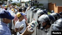 FILE - Opposition supporters hold packages of corn flour in front of riot police during a rally against Venezuelan President Nicolas Maduro's government in San Cristobal, Jan. 23, 2017.