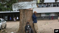 Two men relax under a tree in a poor township on the outskirts of the capital Harare, Nov, 16, 2021.