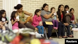 FILE - Migrants sit at the Sacred Heart Catholic Church temporary migrant shelter in McAllen, Texas, June 27, 2014.
