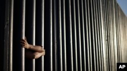 FILE - The hands of Daniel Zambrano of Tijuana, Mexico, hold on to the bars that make up the border wall separating the U.S. and Mexico as the border meets the Pacific Ocean in San Diego, June 13, 2013.