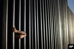 FILE - In this June 13, 2013, photo, hands from Daniel Zambrano of Tijuana, Mexico, hold on to the bars that make up the border wall separating the U.S. and Mexico as the border meets the Pacific Ocean in San Diego.