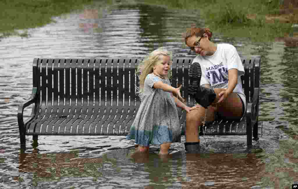 Katie Bender gets some assistance from Johanna Bender (L) as they dump water from a boot while sitting on a flooded street after Hurricane Arthur passed through in Manteo, N.C.