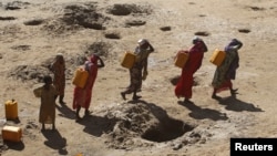 FILE - Women carry jerry cans of water from shallow wells dug from the sand along the Shabelle River bed, which is dry due to drought in Somalia's Shabelle region, March 19, 2016. 