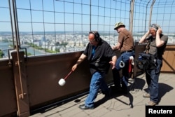U.S. composer Joseph Bertolozzi (L) makes sounds by striking the surface of the Eiffel Tower for a musical project called 'Tower music' June 7, 2013. At right, sound engineer Paul Kozel.hr