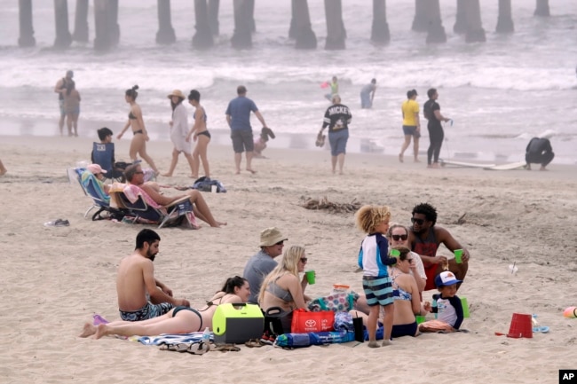 People sit on the beach Sunday, April 26, 2020, in Huntington Beach, Calif.