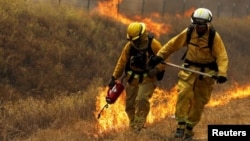 FILE - A California Department of Forestry and Fire Protection (Cal Fire) firefighter sets a backfire with a driptorch along Highway 20 at the Rocky Fire near Lower Lake, California, Aug. 3, 2015. 
