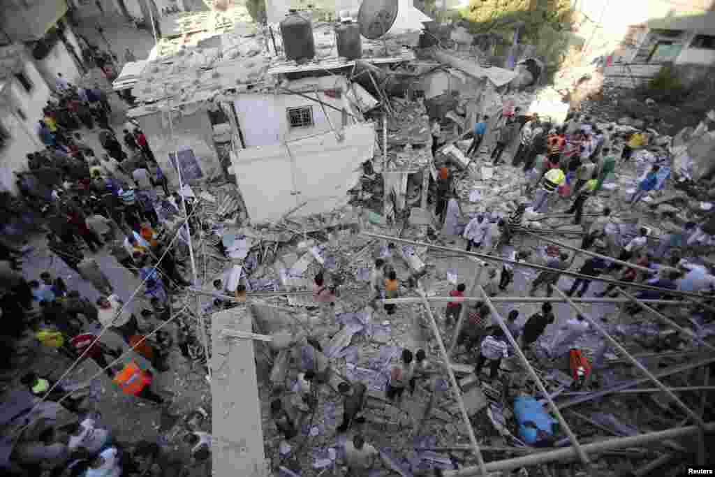 Rescue workers search for victims as Palestinians gather around the wreckage of a house, which witnesses said was destroyed in an Israeli airstrike that killed at least nine members from the al-Ghol family, in Rafah, southern Gaza Strip, August 3, 2014. 