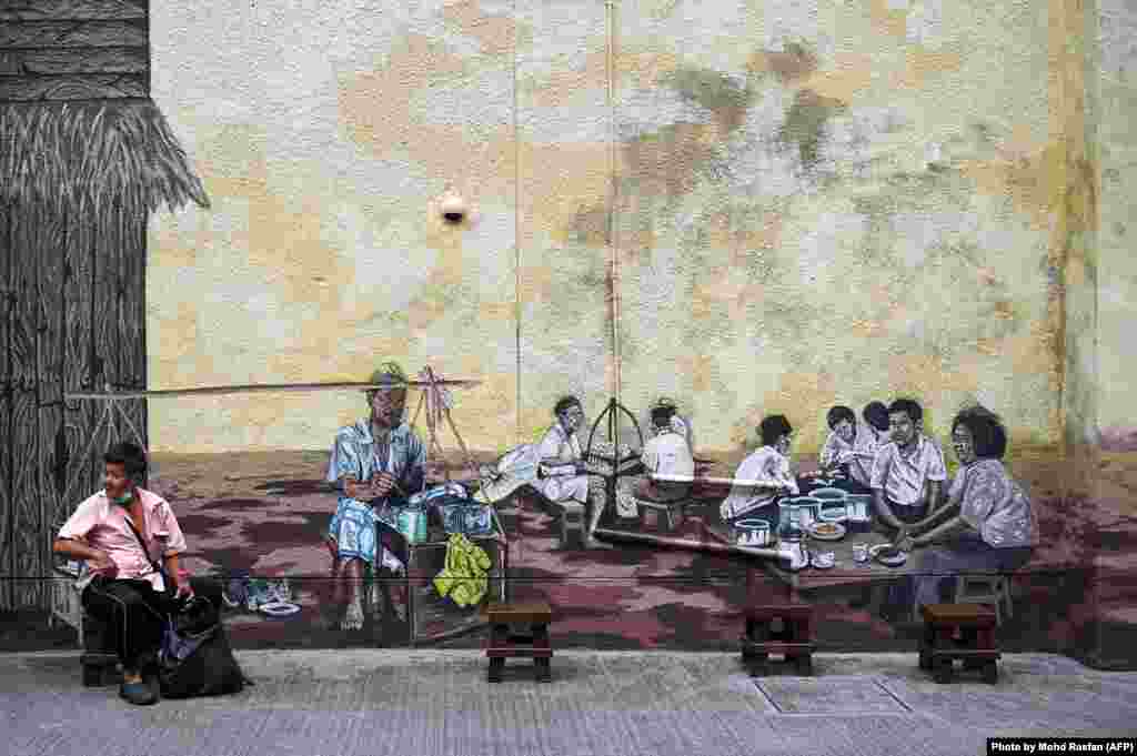 A man sits in front of a mural in Kuala Lumpur, Malaysia.