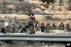 Israeli security forces stand at the scene of an alleged attack at Halhul checkpoint near Hebron, West Bank, Friday, Dec. 11, 2015, after troops shot and killed a Palestinian man who attempted to ram his car into Israeli security forces, military said.