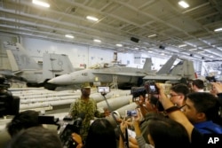 With fighter jets in the background, Lt. Cmdr. Tim Hawkins talks to the media on board the USS Carl Vinson aircraft carrier anchored off Manila, Philippines, for a five-day port call along with guided-missile destroyer USS Michael Murphy, Feb. 17, 2018.