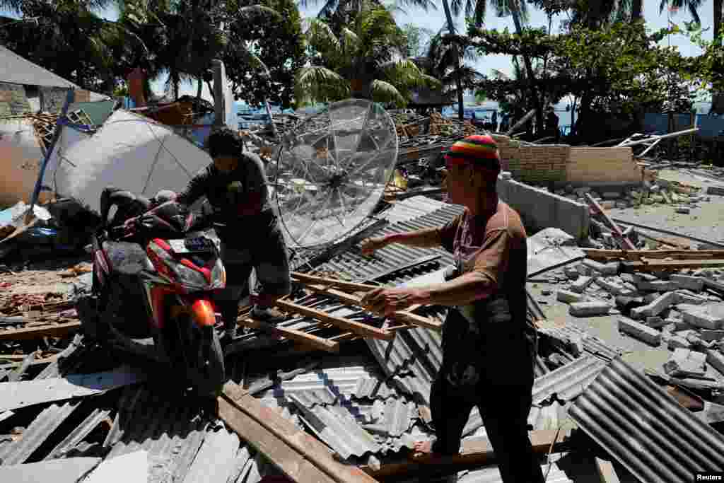 인도네시아 휴양지인 롬복에서 6.9 규모의 지진이 발생한 가운데 마을 주민들이 무너진 건물 잔해 사이에서 오토바이를 밀고 있다.