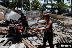 5일 인도네시아 휴양지인 롬복에서 6.9 규모의 지진이 발생한 가운데 마을 주민들이 무너진 건물 잔해 사이에서 오토바이를 밀고 있다.