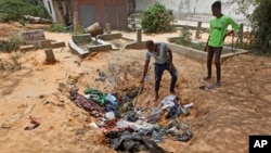 Afrah Ibrahim, center, searches through the clothes of the dead lying in a hole, to try and find the clothes last worn by his missing sister, without success, outside a hospital in Mogadishu, Somalia, Oct. 17, 2017. 