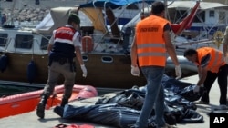 A Turkish paramilitary officer and local workers collect the bodies of migrants after coast guard officials said 13 migrants died after their boat collided with a ferry off the Turkish coast near Ayvacik, Canakkale, Turkey, Sept. 20, 2015. 